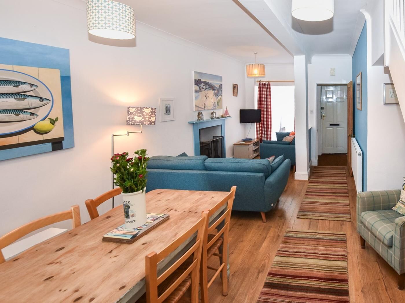 A modern living room with a blue sofa, wooden dining table, and a TV.