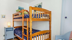 Ein Stockbett mit Holzrahmen, ein kleiner Nachttisch mit Lampe, ein Stuhl und eine Wand mit einem gerahmten Bild.