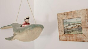 Eine Skulptur zeigt eine Figur in einem Boot und ein gerahmtes Bild einer Küstenlandschaft.