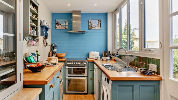 Eine kompakte Küche mit Herd, Backofen und Waschmaschine, Holz Arbeitsplatten und einer blauen Wand.