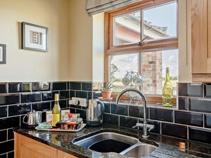 A kitchen with a black tiled backsplash, stainless steel sink, and a window with a view of a brick building. - 1 Bed in York (oc-92093) (High Catton)
