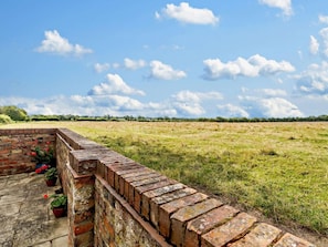 A brick wall with potted plants, a grassy field, and a clear sky with clouds. - 1 Bed in York (oc-92093) (High Catton)