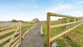 Un chemin de gravier mène à une structure en bois, avec un portail en métal sur la gauche et une clôture en bois sur la droite.