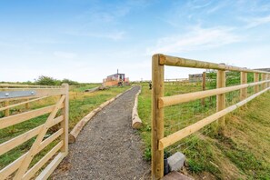 A gravel path leading to a wooden structure with a metal gate on the left and a wooden fence on the right.