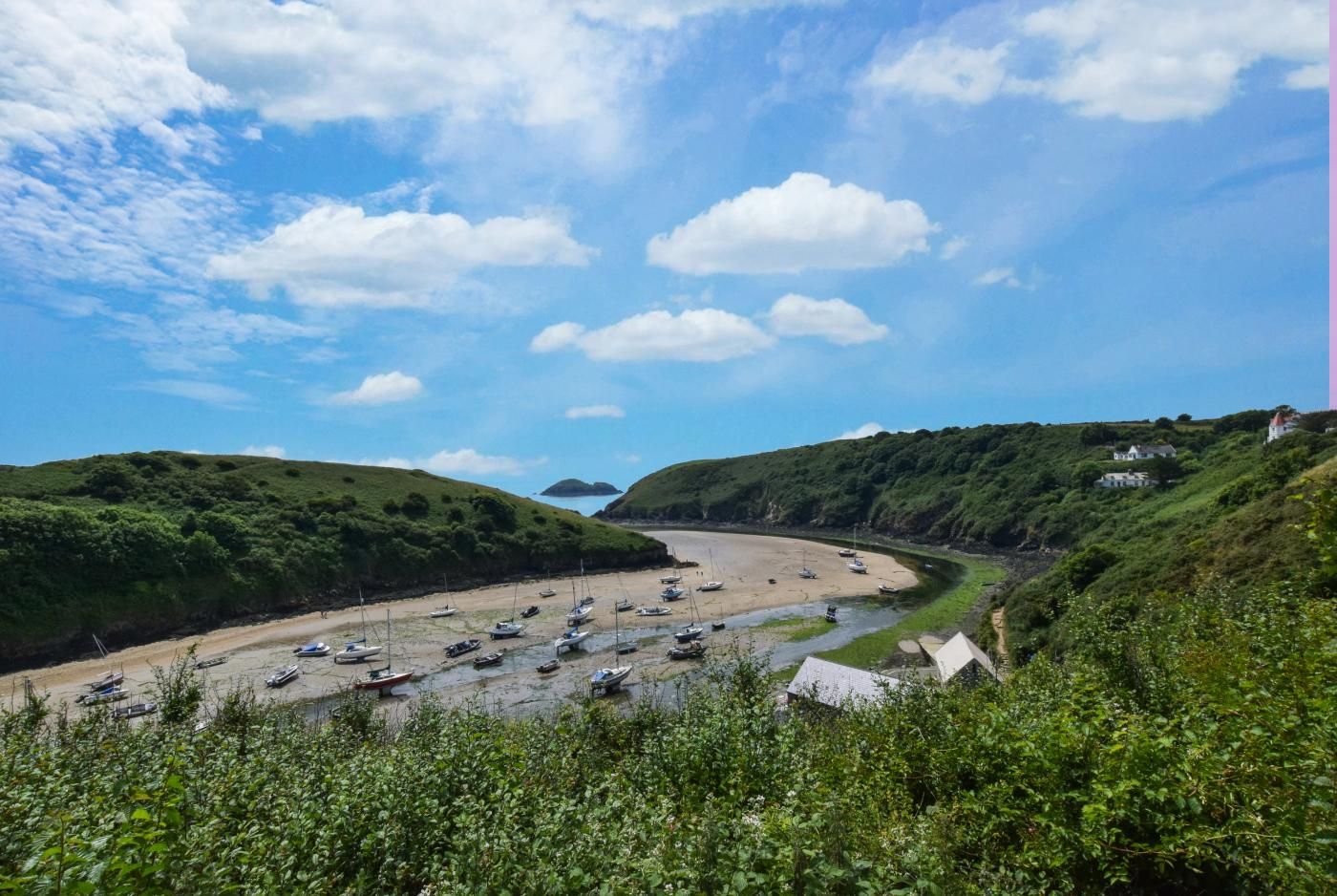 A coastal landscape with boats on a sandy beach, surrounded by green hills and a clear sky.