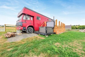 A red camper van parked on a gravel path with a wooden structure nearby.
