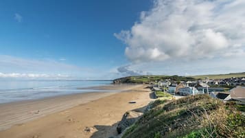 Une plage côtière avec un rivage sablonneux, une rangée de maisons et un grand nuage dans le ciel.