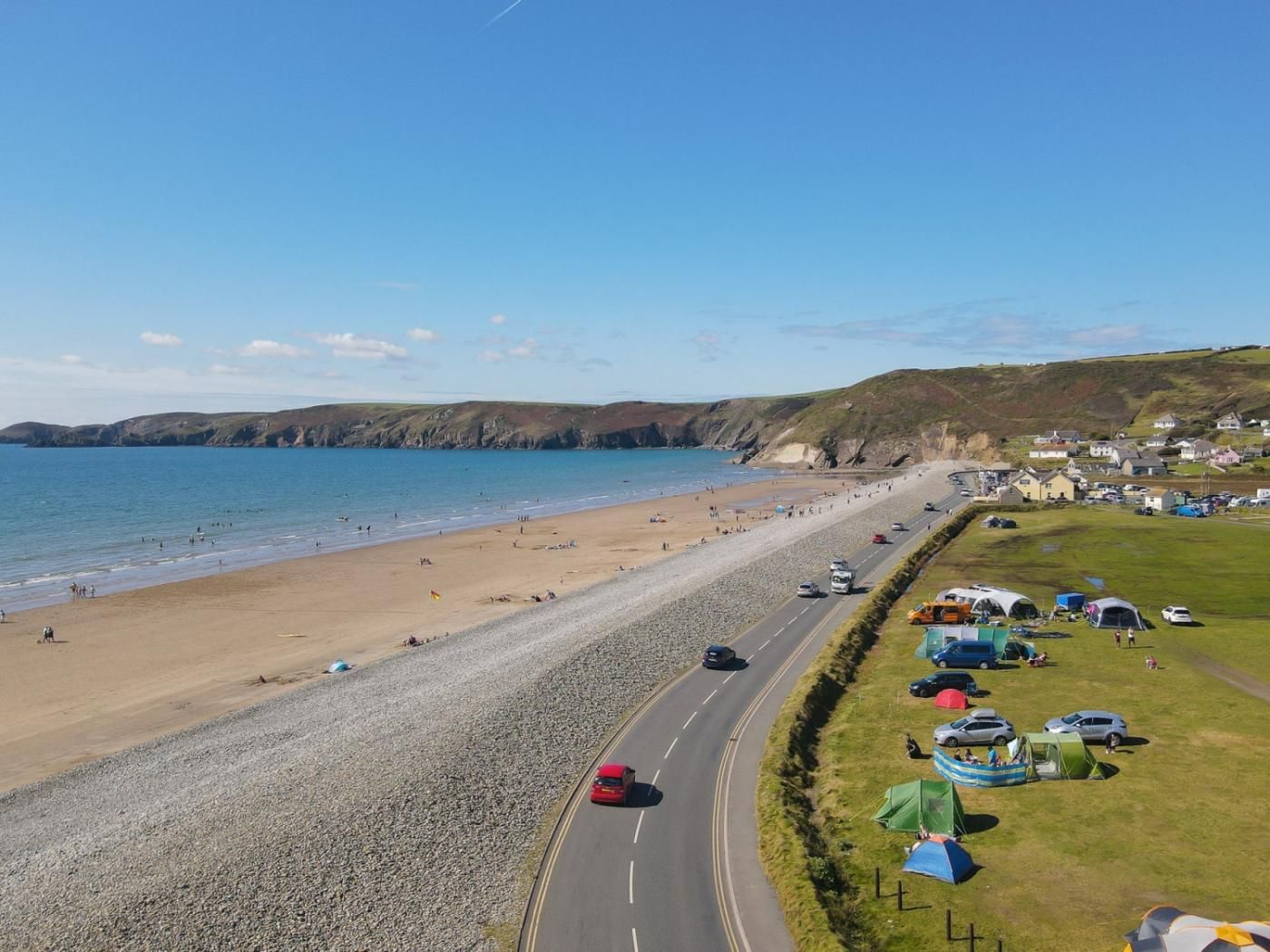Une route côtière donnant accès à la plage, avec des véhicules et des tentes stationnés le long de celle-ci.