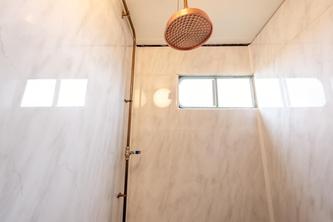 Een douche met een handdouche, een raam en een deur met een handdoekhouder.