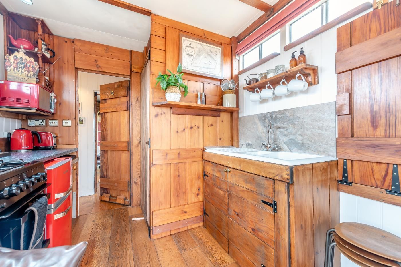 A compact kitchen with wooden cabinets, a red stove, and a sink.