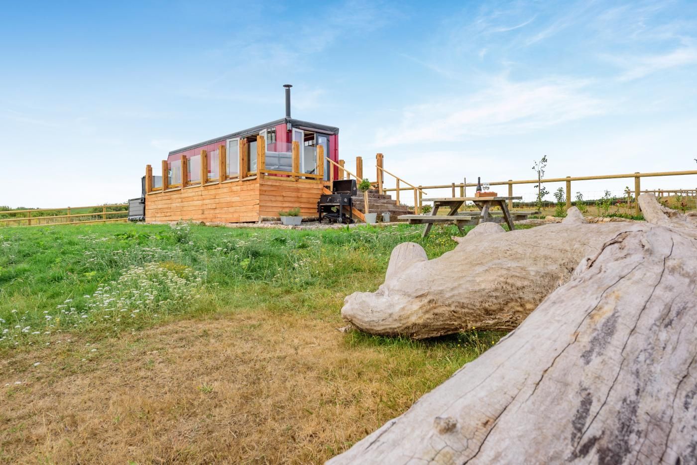 A wooden cabin with a chimney, a picnic table, and a large log in the foreground.