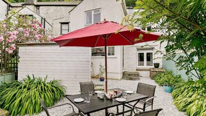 A patio with a table set for two, a red umbrella, and a white fence. - 3 Bed in Looe (oc-92273) (Polperro)