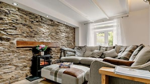 A cozy living room with a stone wall, a sofa, an ottoman, and a table with a book. - 3 Bed in Looe (oc-92273) (Polperro)