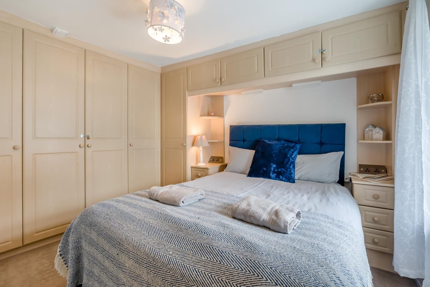 A bedroom with a bed, nightstands, a lamp, a headboard, and a wardrobe.