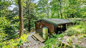 A small wooden cabin with a porch, surrounded by dense forest. - 2 Bed in Ambleside (oc-92240) (Grasmere)