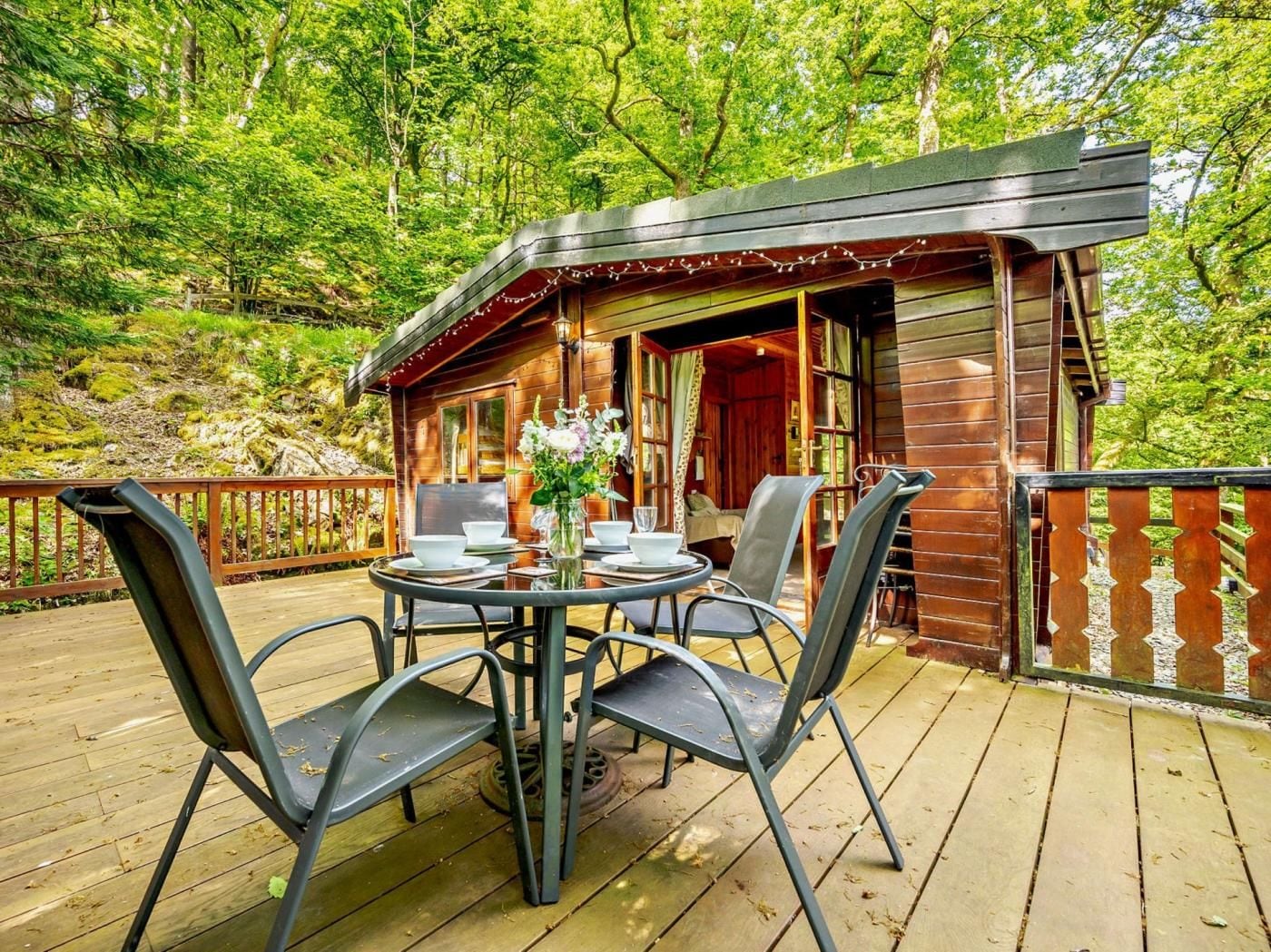 A wooden cabin with a deck, surrounded by trees.