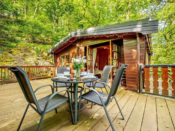 A wooden cabin with a deck, surrounded by trees.