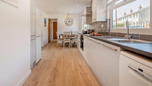 A modern kitchen with white cabinetry, a wooden floor, a dining area with a table and chairs, and a view of buildings through a window. - 3 Bed in Wareham (oc-92328) (West Lulworth)