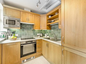 Eine Küche mit Holzausstattung, einer Edelstahl-Mikrowelle, einem Einbauofen und einer grünen Fliesenrückwand.