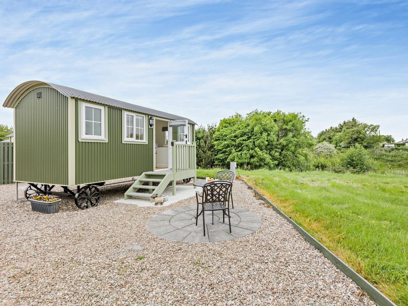 A green mobile home with a porch, a table, and chairs outside.