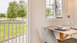 Ein Essbereich mit einem Tisch für zwei Personen, ein Fenster mit Blick auf Bäume und ein Balkon mit Geländer.