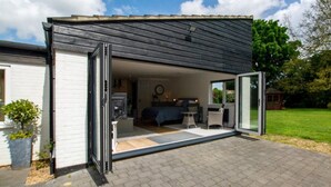 A modern house with a patio, a dining area, and a kitchen visible through an open door. - 1 Bed in Norwich (oc-92295) (Strumpshaw)