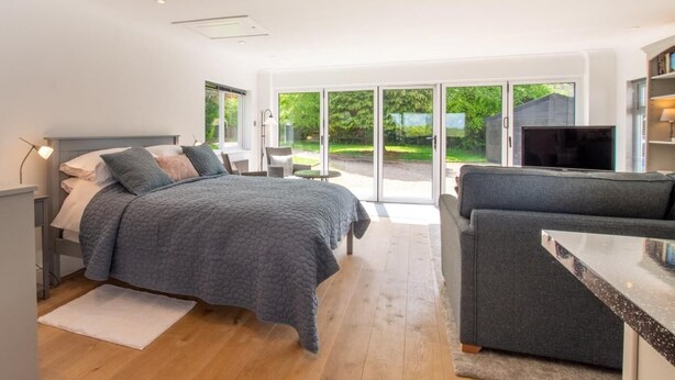 A modern bedroom with a bed, a TV, and a seating area with a view of the outdoors. - 1 Bed in Norwich (oc-92295) (Strumpshaw)