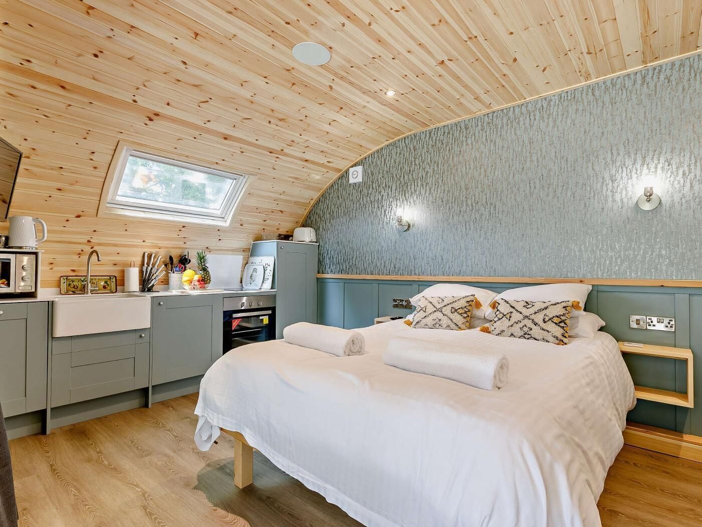 Une chambre confortable avec un plafond en bois, un lit avec une literie blanche, une petite kitchenette et une fenêtre.