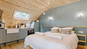 Une chambre confortable avec un plafond en bois, un lit avec une literie blanche, une petite kitchenette et une fenêtre.