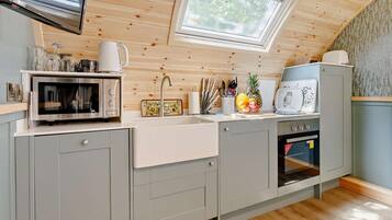 Une cuisine moderne équipée d’un four à micro-ondes, d’un four et d’un évier intégrés. Un puits de lumière se trouve au-dessus de l’évier, et la cuisine est dotée d’un plafond en bois.