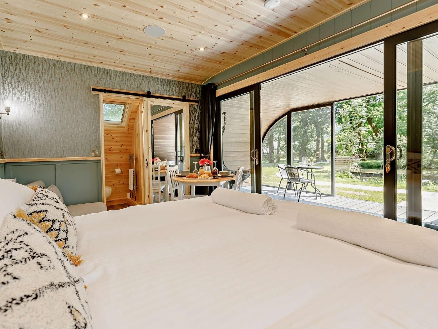 Une chambre avec un grand lit, une table à manger avec des chaises et une vue sur l’extérieur.