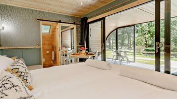 A bedroom with a large bed, a dining table with chairs, and a view of the outdoors.