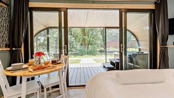 Une chambre avec un lit, une table à manger avec des chaises, un coin pour prendre le petit-déjeuner et une vue sur l’extérieur, accessible par une porte vitrée.