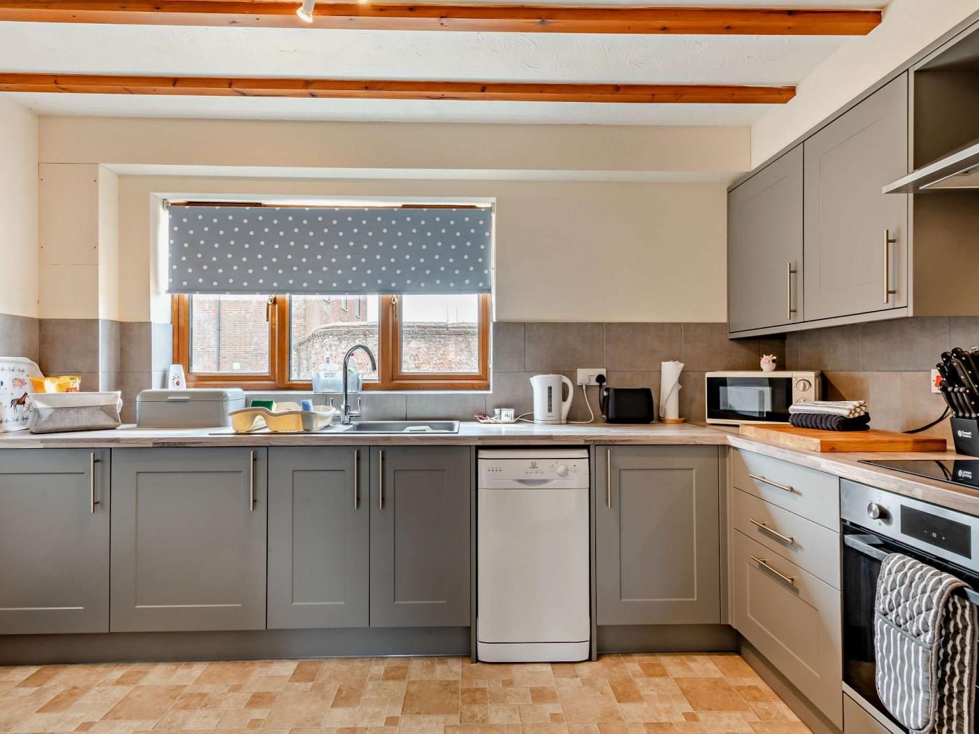 A modern kitchen with grey cabinets, a dishwasher, a microwave, and a window with a polka dot curtain.
