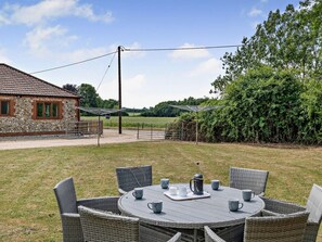 A round outdoor table with wicker chairs, a stone building with a tiled roof, and a metal fence. - 2 Bed in Dereham (oc-92392) (Horningtoft)