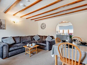 A cozy living room with a sofa, a small table with tea set, a wooden chair, and a kitchen visible through an archway. - 2 Bed in Dereham (oc-92392) (Horningtoft)