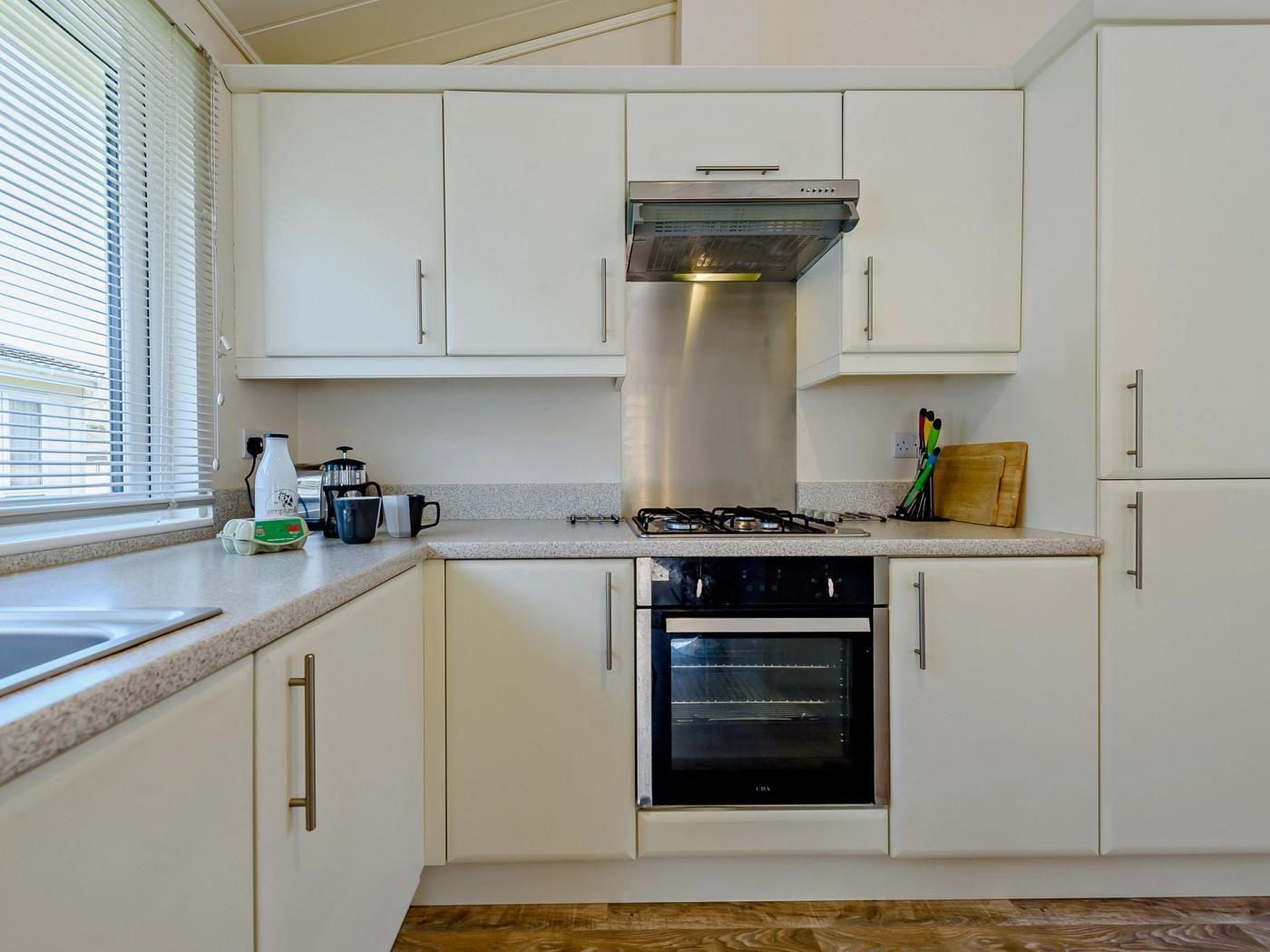 A kitchen with white cabinets, a stainless steel range hood, a built-in oven, and a window with blinds.