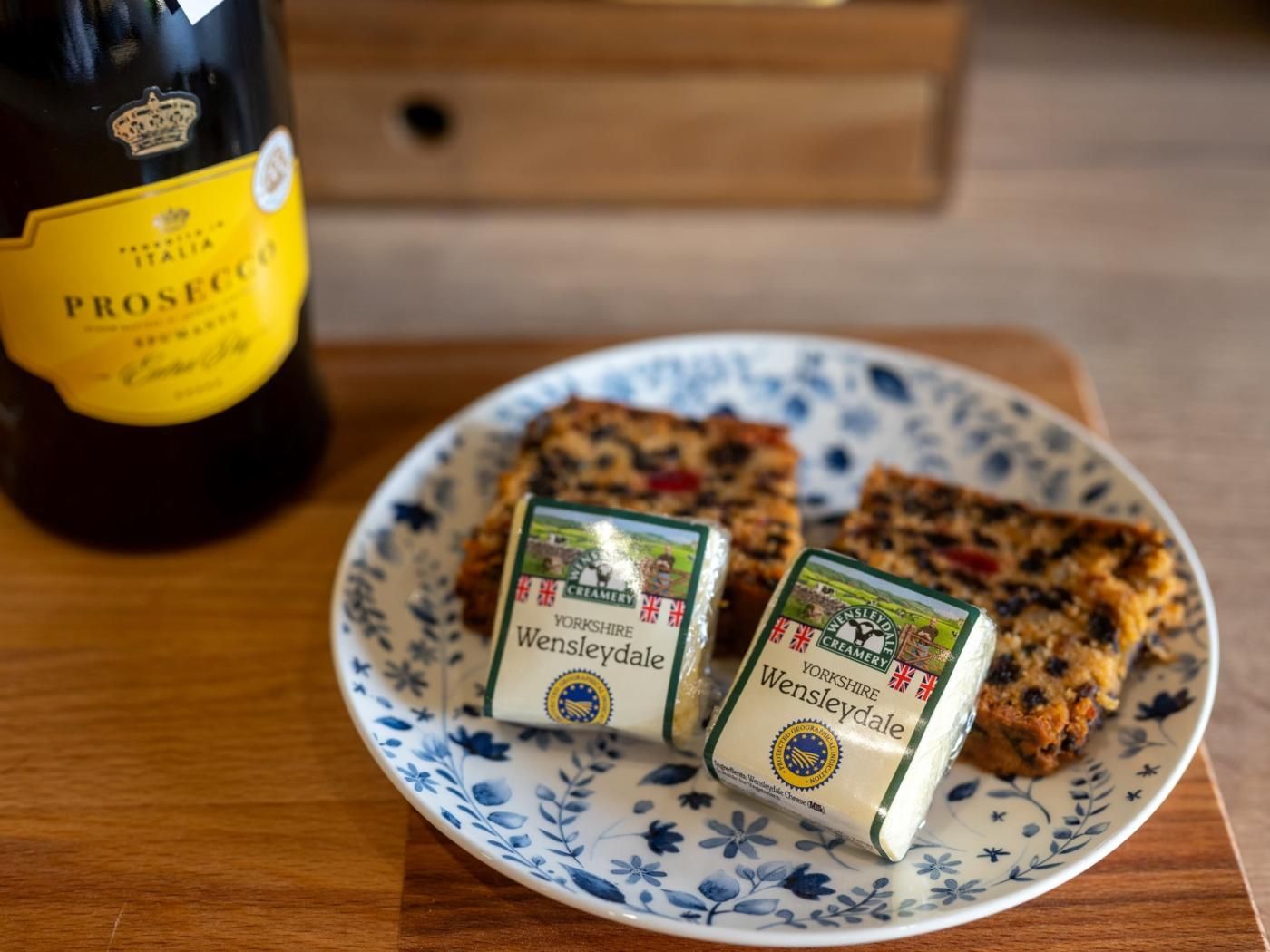 Eine Flasche Prosecco und zwei Portionen Wensleydale-Creme-Käse auf einem blumengedeckten Teller.