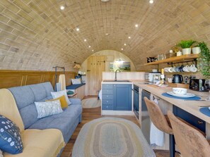 Een compacte keuken met een centraal eiland, een zithoek met een bank, en een keukentafel met diverse apparaten en keukengerei.