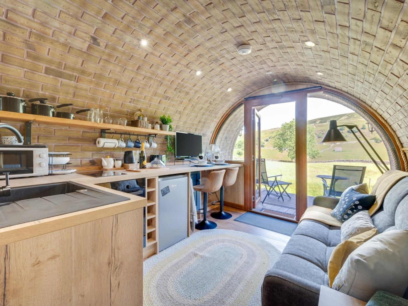 A cozy kitchen with a brick ceiling, a dining area with a sofa and table, and a view of the outdoors through a glass door.