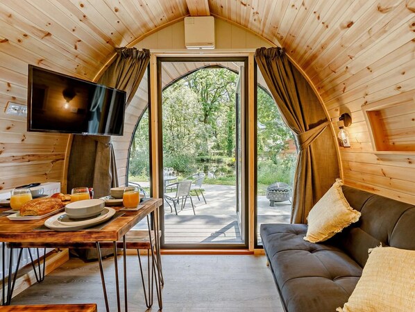 A cozy room with a wooden interior, a television, a dining table with breakfast items, and a sofa with cushions.
