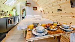 A cozy cabin with a kitchen, a dining area with breakfast, and a bed with white linens.