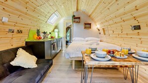A cozy cabin interior with a wooden ceiling, a kitchenette, a dining area with breakfast, and a comfortable seating area.