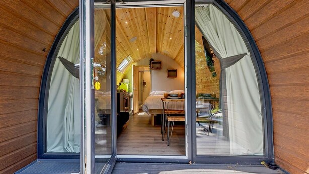 A modern, semi-open structure with a wooden interior, a dining area, and a visible bedroom.