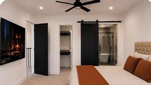 Une chambre à coucher comprenant un lit, un ventilateur de plafond, un placard à portes coulissantes et une salle de bain avec une douche en verre.