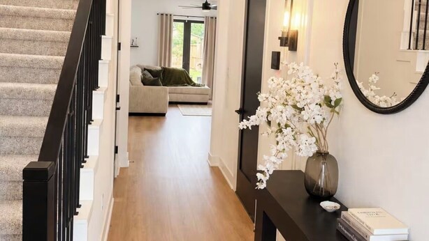 Un couloir avec un escalier, une console sur laquelle sont posés un vase et des livres, et un grand miroir.