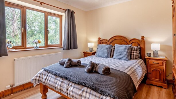 Ein Schlafzimmer mit einem hölzernen Bett, zwei Nachttischen, einem Fenster mit Vorhängen und einer Heizung.