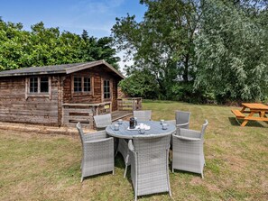 Une cabane en bois dotée d’une terrasse et d’une table ronde entourée de chaises, le tout situé dans un espace verdoyant.