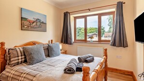Ein Schlafzimmer mit einem Bett, einem Gemälde, einem Fenster mit Vorhängen und einem Fernseher.