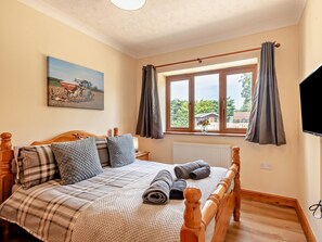Ein Schlafzimmer mit einem Bett, einem Gemälde, einem Fenster mit Vorhängen und einem Fernseher.